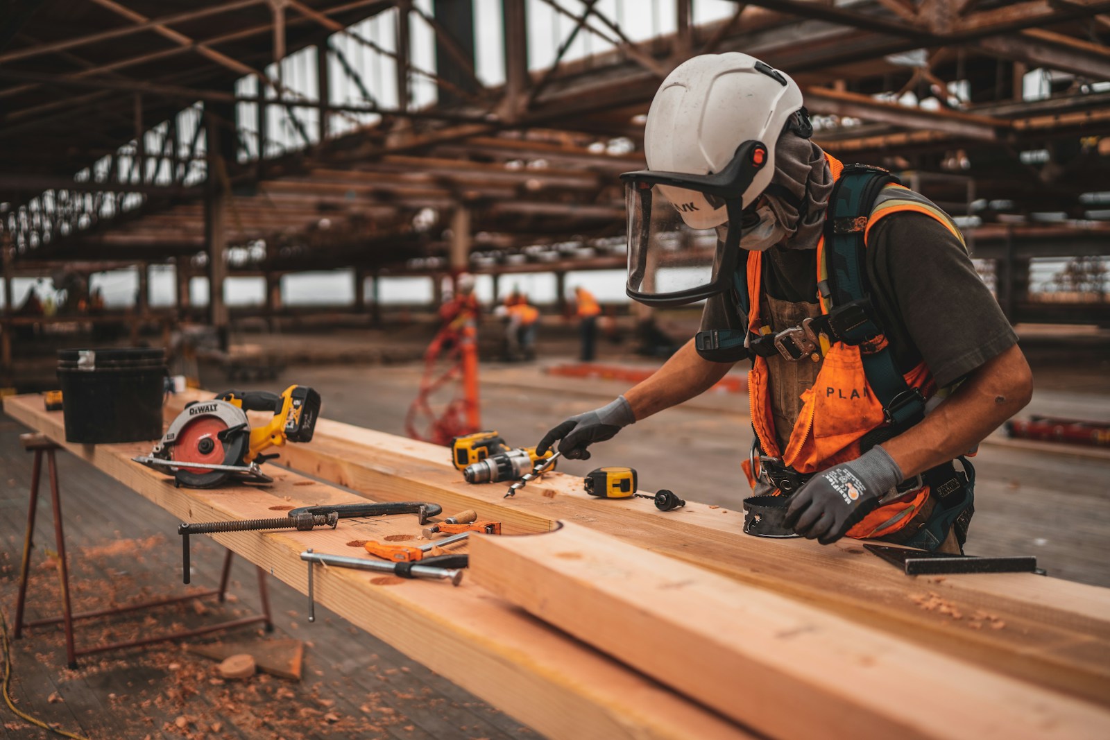 man in orange and black vest wearing white helmet holding yellow and black power tool, workers